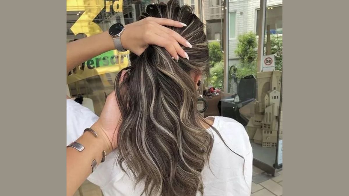 nau-tay-lanh-9 Người đang chạm vào tóc màu nâu dài có lọn sáng, đứng trong không gian nội thất với cửa kính lớn.