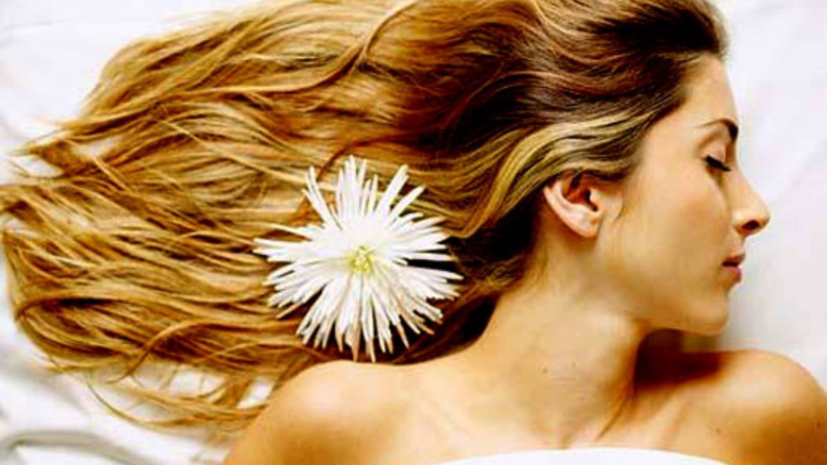 nhuom-balayage-toc-ngan-10 Người với mái tóc dài nâu vàng, có hoa trắng cài bên tóc, đang nằm nghiêng trên bề mặt trắng.