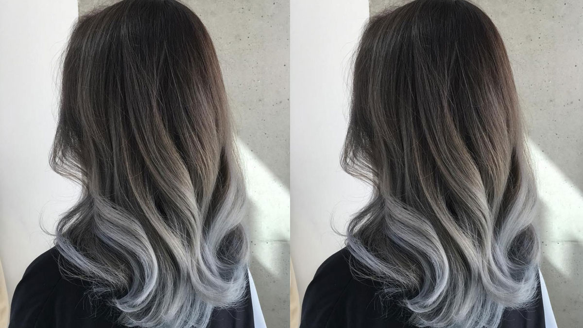 Tóc dài uốn lượn với màu nhuộm ombre từ nâu đậm đến xám nhạt, chụp từ phía sau trong ánh sáng tự nhiên.