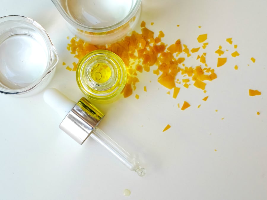 Lọ dầu và pipet trên bàn với mảnh vụn màu vàng và cốc thủy tinh đựng chất lỏng trong suốt.