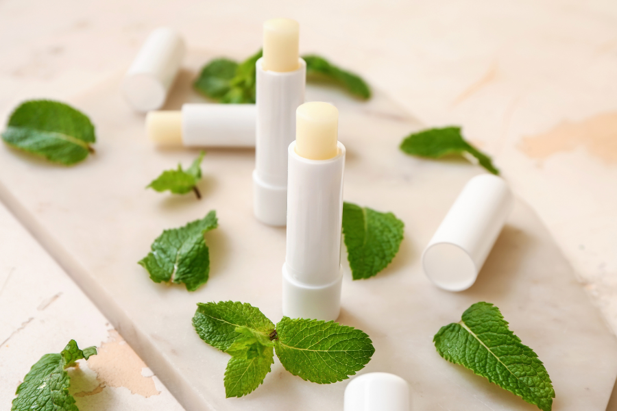 Thỏi son dưỡng môi trên nền trắng, xung quanh có lá bạc hà tươi.