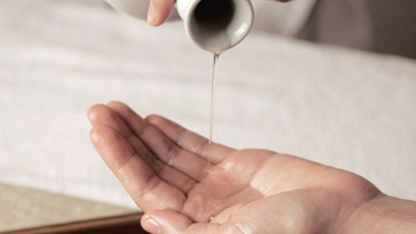 Người đang đổ dầu từ một b&igrave;nh nhỏ v&agrave;o l&ograve;ng b&agrave;n tay, chuẩn bị cho một liệu ph&aacute;p m&aacute;t-xa.