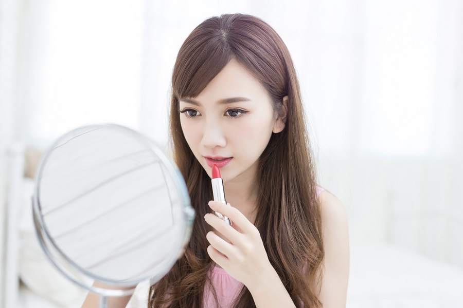 Người phụ nữ soi gương và thoa son môi đỏ trong không gian sáng sủa.