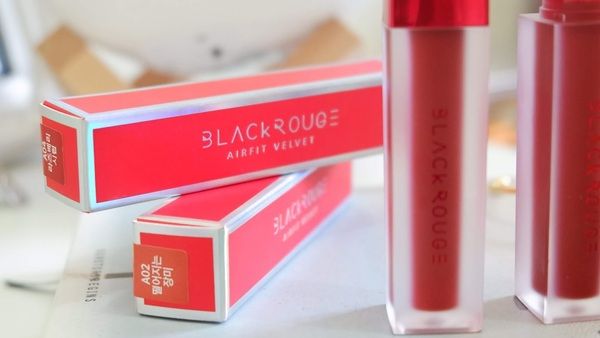 Hộp và thỏi son màu đỏ với chữ "BLACK ROUGE AIRFIT VELVET" trên bề mặt, đặt trên nền sáng.
