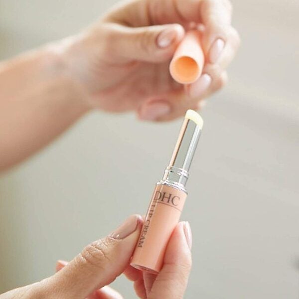son_dhc_khong_mau_cho_hieu_qua_duong_moi_vuot_troi_72c5fb90843240d3bd757e7508a95003_grande Người đang mở nắp thỏi son dưỡng môi màu hồng nhạt trong tay.