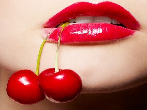 Đôi môi đỏ, căng mọng đang ngậm hai quả cherry đỏ tươi, tạo nên hình ảnh ấn tượng và gợi cảm.