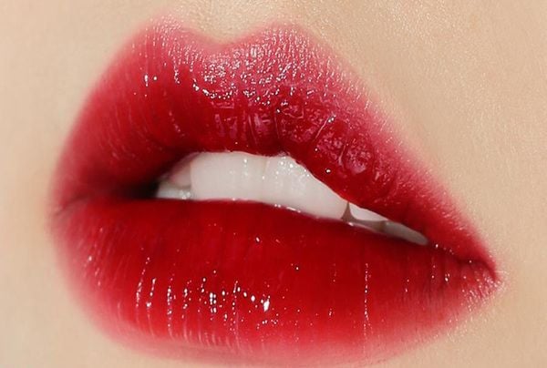 Đôi môi tô son đỏ đậm, bóng và mịn màng, ánh sáng phản chiếu làm nổi bật sắc đỏ.