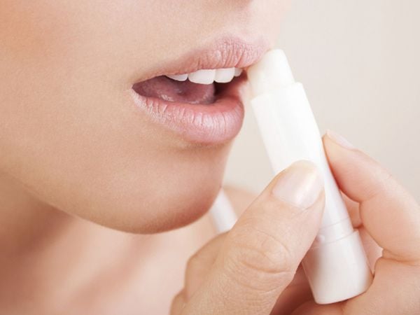 Người đang thoa son dưỡng l&ecirc;n m&ocirc;i với tay cầm thỏi son m&agrave;u trắng.