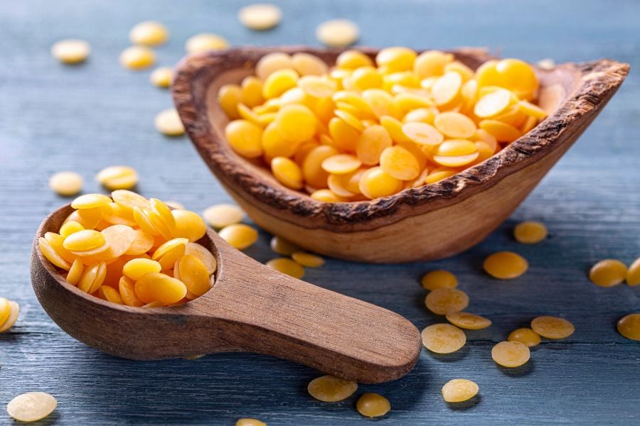 Hạt màu vàng trong bát gỗ và muỗng gỗ trên nền xanh.