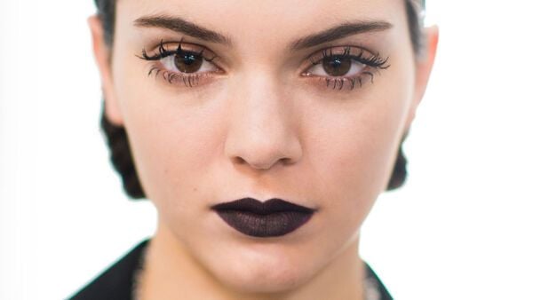 Người phụ nữ trang điểm đậm với son m&ocirc;i đen v&agrave; l&ocirc;ng mi d&agrave;i, nh&igrave;n thẳng v&agrave;o ống k&iacute;nh.