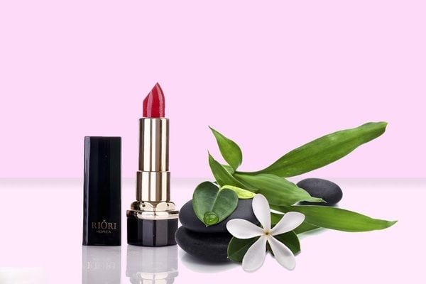 Thỏi son đỏ cạnh đá và lá cây xanh, nền hồng nhạt, tạo cảm giác tự nhiên và tinh tế.