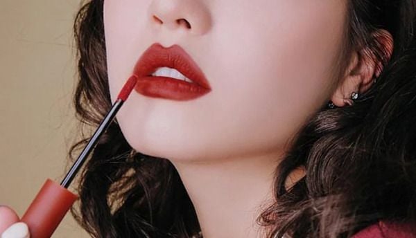 Người đang thoa son môi đỏ, tóc xoăn nhẹ, không nhìn thấy toàn bộ khuôn mặt.