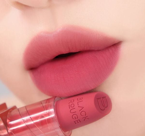 Đôi môi tô son màu hồng, cận cảnh với thỏi son màu tương tự được cầm gần đó.