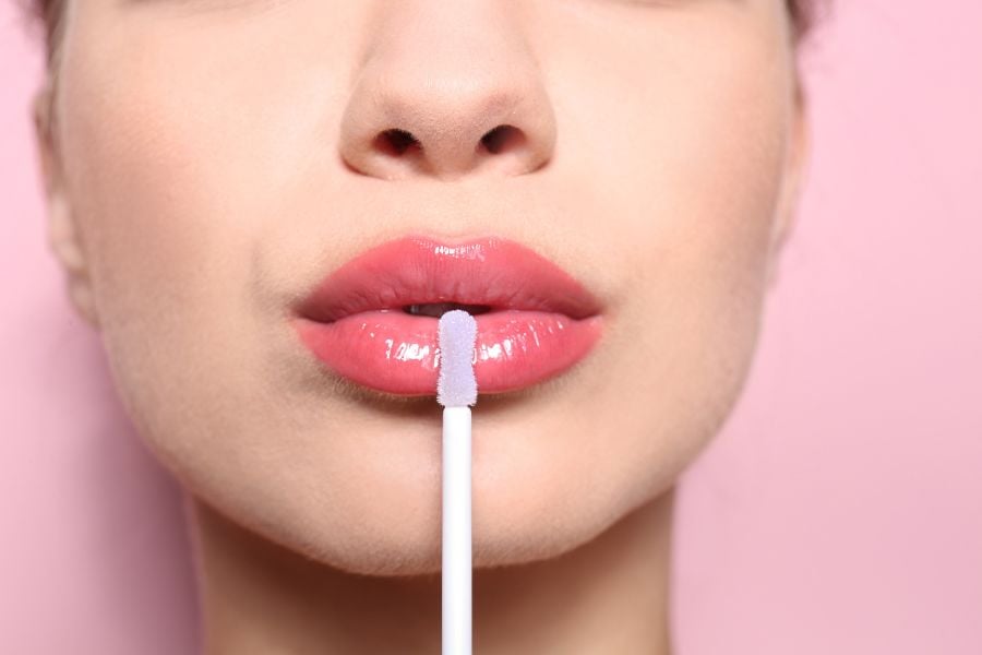 Người đang thoa son môi màu hồng, nền màu hồng nhạt, cận cảnh đôi môi.