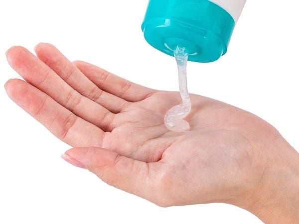 Một tay hứng gel trong suốt được bóp ra từ chai nhựa xanh dương và trắng.