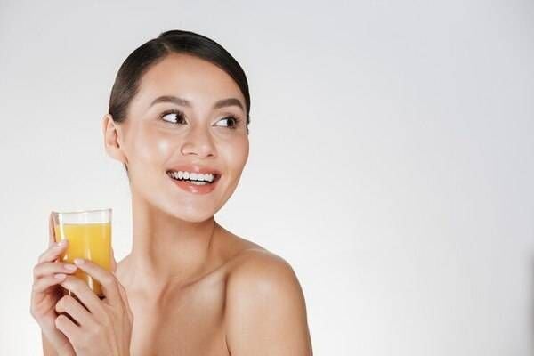 Người phụ nữ cầm ly nước cam, cười tươi, nền trắng đơn giản.
