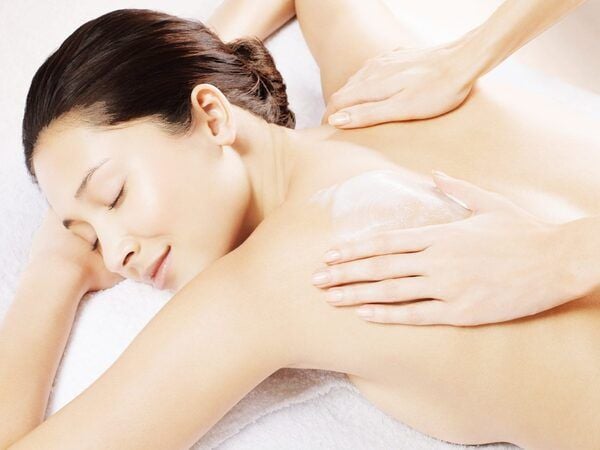 Người đang được massage thư giãn với kem dưỡng trên lưng, nằm trên khăn trắng, mắt nhắm.