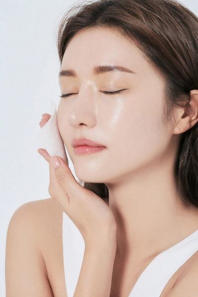 Người phụ nữ nhắm mắt, tay chạm má, làn da sáng bóng, nền trắng.