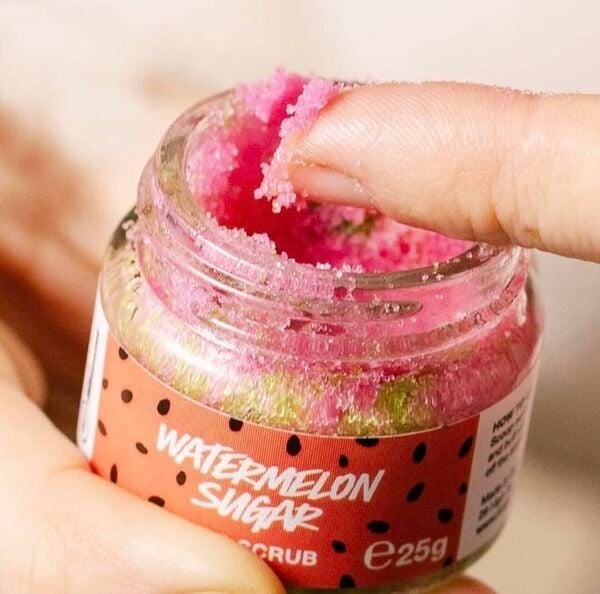 Người đang lấy một &iacute;t muối tẩy tế b&agrave;o chết m&agrave;u hồng từ hũ nhỏ c&oacute; nh&atilde;n "Watermelon Sugar".