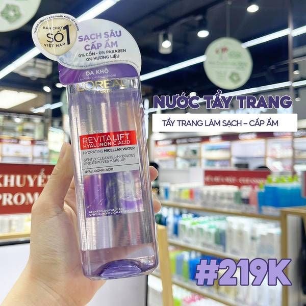 tay_trang_diu_nhe__giup_loai_bo_toi_93_8_can_trang_diem_55d21e7485914b5092c1ebd75c8f6312_grande Chai nước tẩy trang được cầm trên tay, nền là kệ hàng hóa trong một cửa hàng mỹ phẩm.