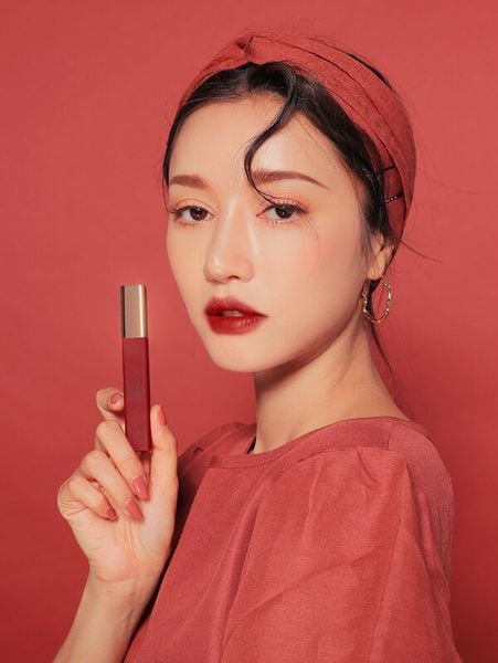 Người phụ nữ cầm thỏi son đỏ, mặc áo và băng đô cùng tông màu, nền đỏ hài hòa.