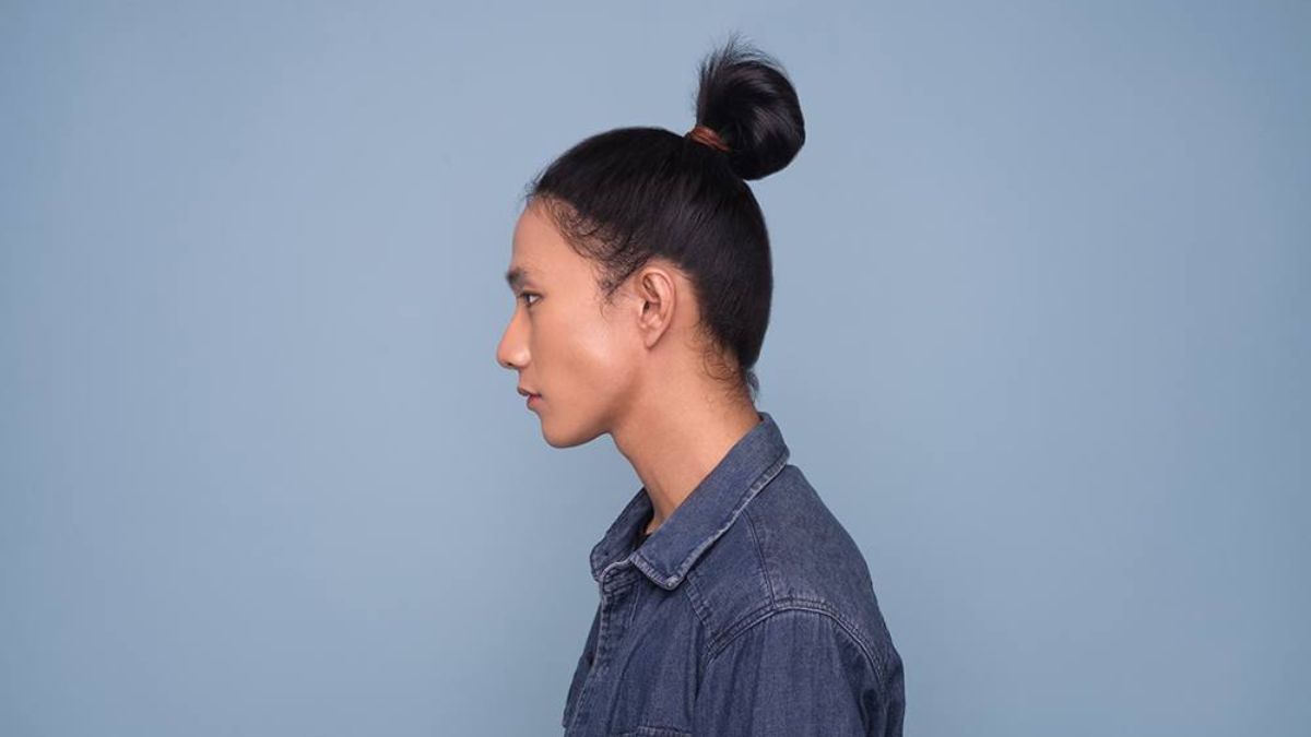 toc-buoc-nam-3 Người đang nhìn ngang, tóc búi, mặc áo denim, trên nền xanh nhạt.
