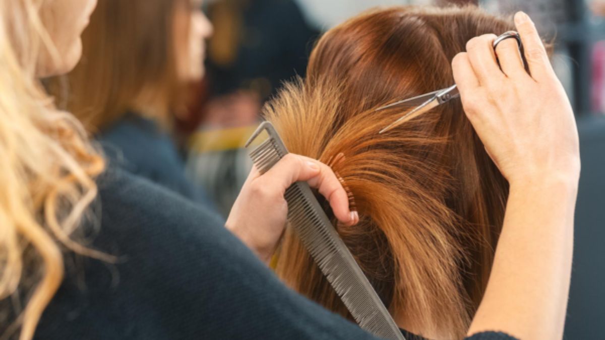 Người thợ cắt tóc đang dùng kéo và lược để cắt tóc cho khách hàng trong tiệm làm tóc.