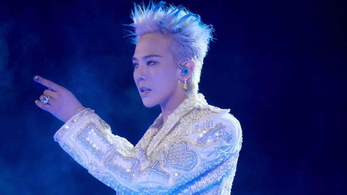 toc-g-dragon-1 Người biểu diễn trên sân khấu trong trang phục trắng lấp lánh, tóc bạch kim, chỉ tay về phía trước.