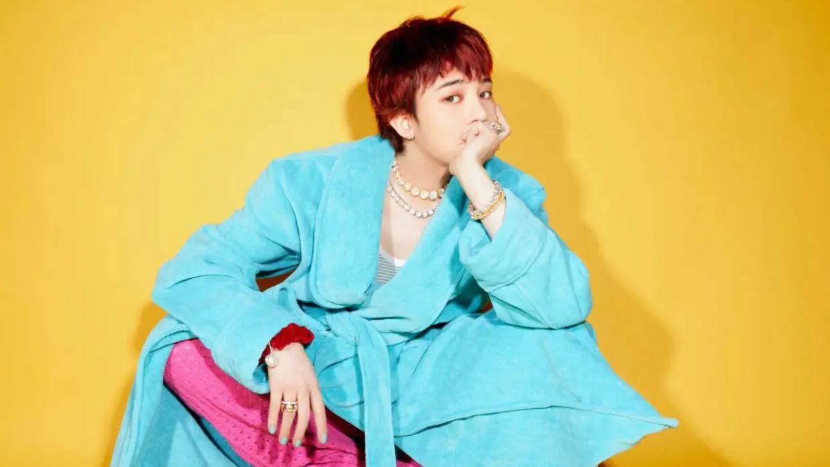 toc-g-dragon-18 Người ngồi trong áo choàng xanh, phông nền vàng, biểu cảm suy tư, trang sức nổi bật.