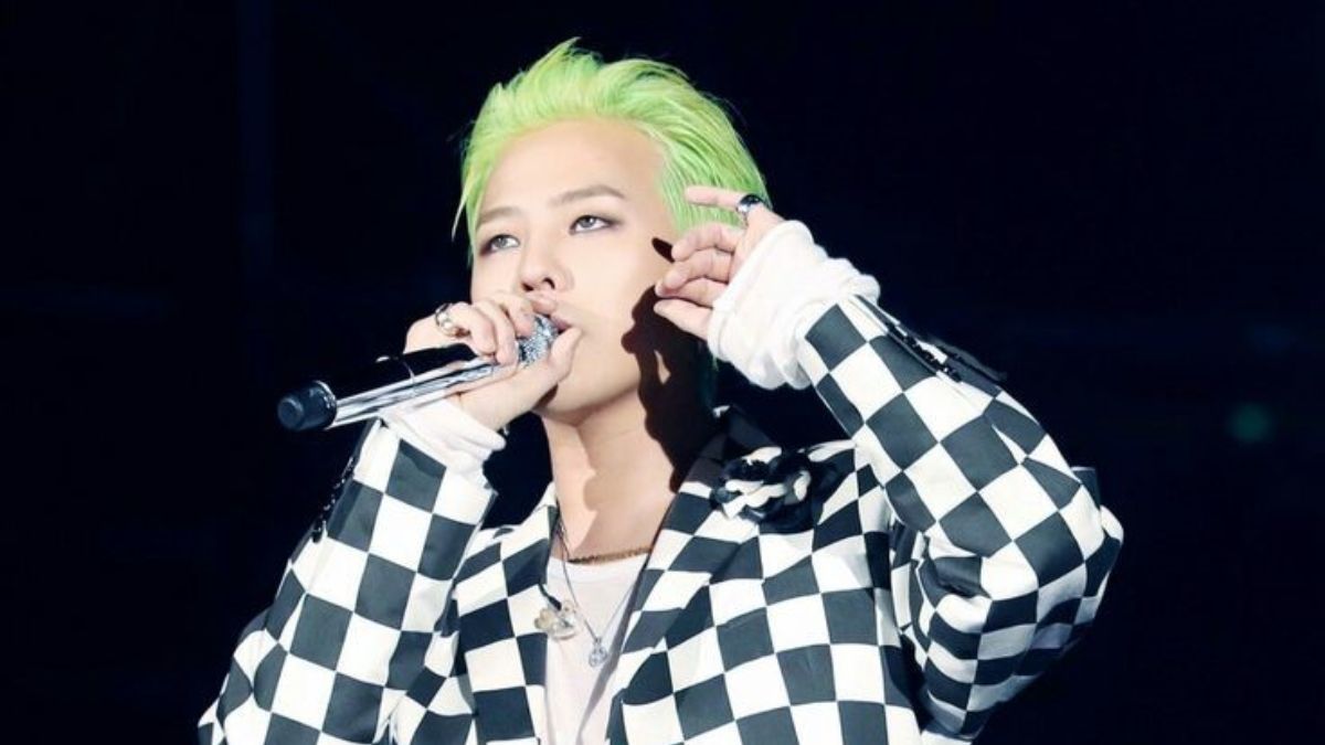 toc-g-dragon-22 Người biểu diễn tóc xanh đang hát trên sân khấu, mặc áo họa tiết ca rô đen trắng, cầm micro.