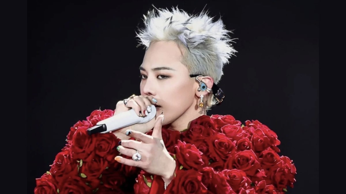 toc-g-dragon-3 Người biểu diễn cầm micro, mặc trang phục hoa hồng đỏ, tóc bạch kim, đứng trên sân khấu.