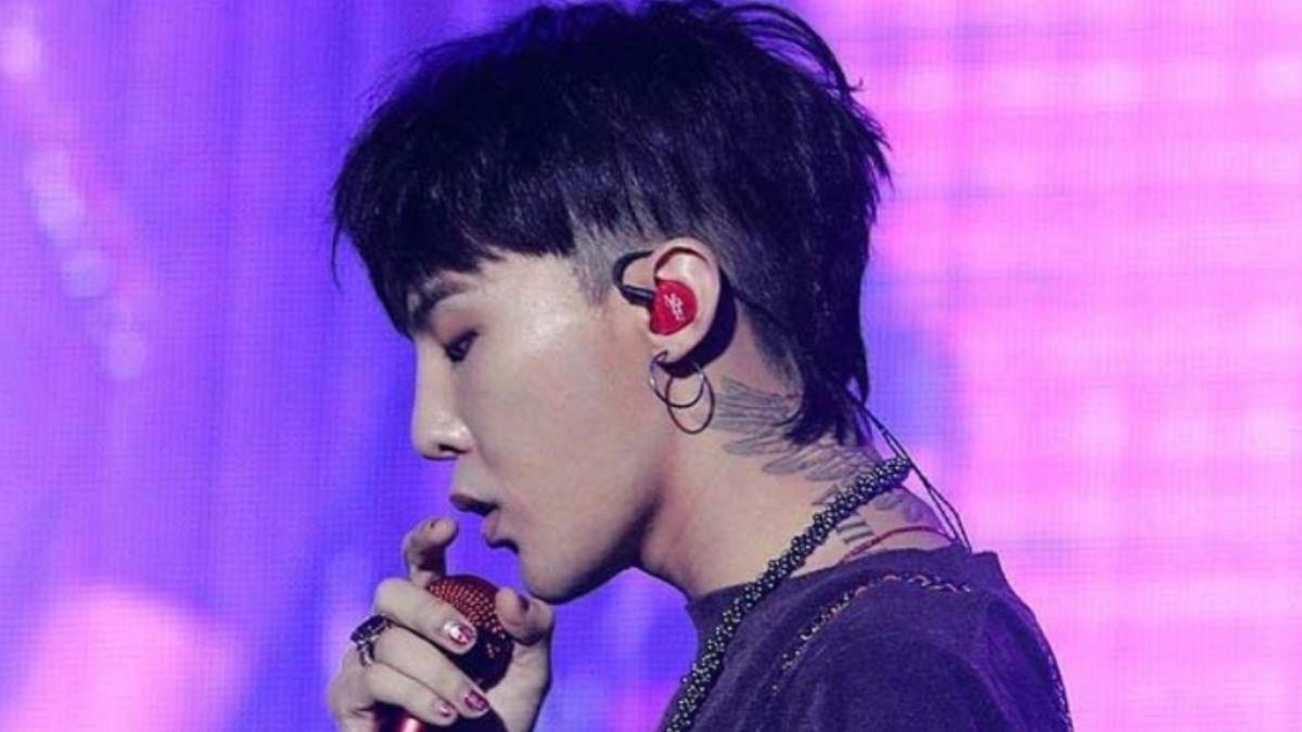 toc-g-dragon-4 Người đang hát trên sân khấu, đeo tai nghe màu đỏ, nền sáng tím.