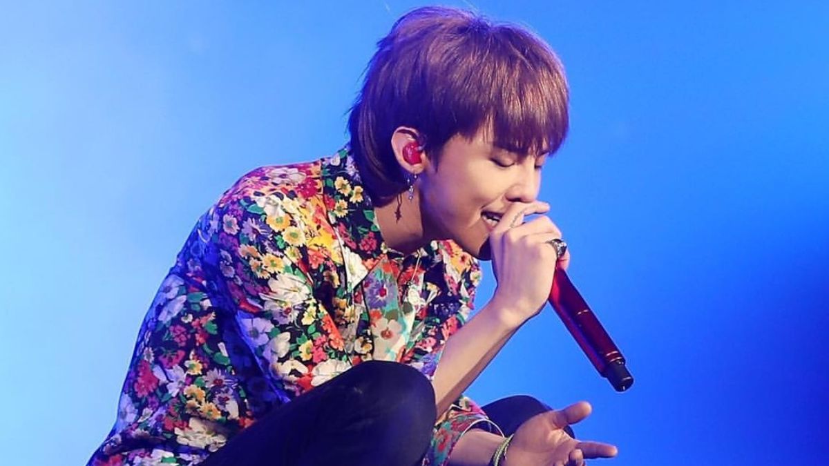 toc-g-dragon-5 Người đang hát trên sân khấu, mặc áo sơ mi hoa và cầm micro đỏ, nền sáng màu xanh.