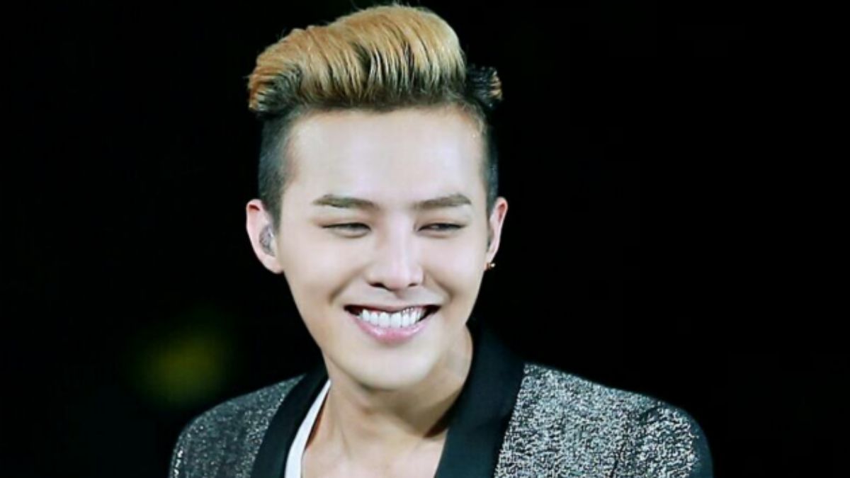 toc-g-dragon-8 Người đang cười, tóc nhuộm sáng, mặc áo khoác lấp lánh, nền tối.