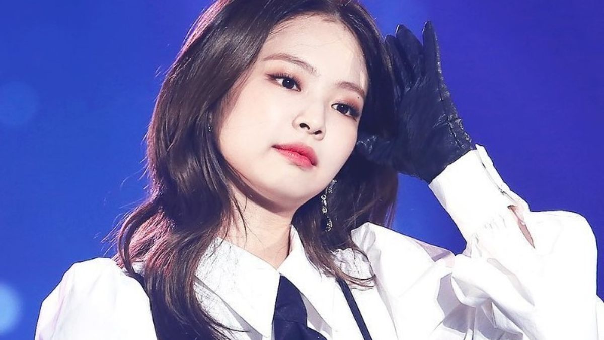 toc-jennie-7 Người phụ nữ mặc áo trắng, đeo găng tay đen đang đứng trên sân khấu với biểu cảm suy tư.