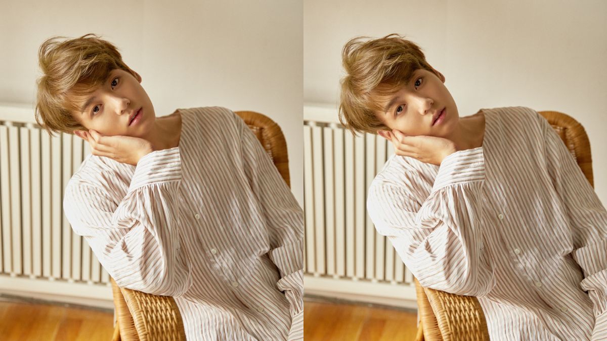 toc-jungkook-13 Người mặc áo sọc, ngồi trên ghế, tay chống cằm, nhìn thẳng vào máy ảnh, trong căn phòng có lò sưởi.