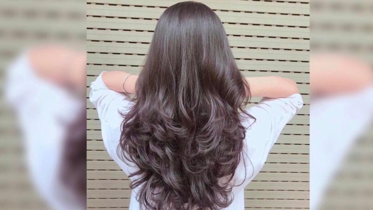Mái tóc dài và xoăn nhẹ của một người đang đứng quay lưng, nền là bức tường sọc ngang.