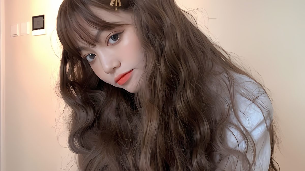 Người phụ nữ với mái tóc dài xoăn, đang nhìn về phía trước trong bối cảnh ánh sáng ấm áp.