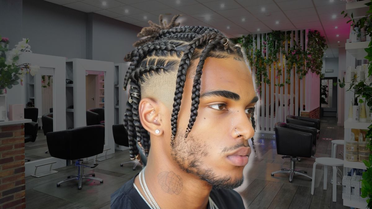 toc-mohawk-14 Người với kiểu tóc tết cầu kỳ đứng trong tiệm làm tóc hiện đại, có ghế và gương, trang trí cây xanh.
