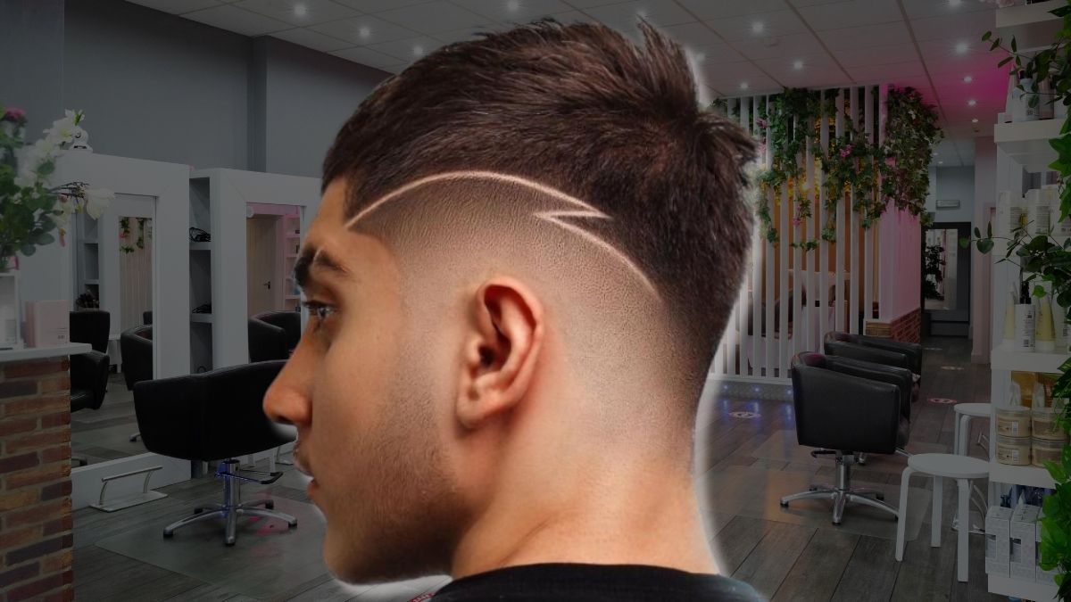 toc-mohawk-15 Người đàn ông với kiểu tóc cạo nghệ thuật trong tiệm làm tóc, nội thất hiện đại với ghế và cây xanh.