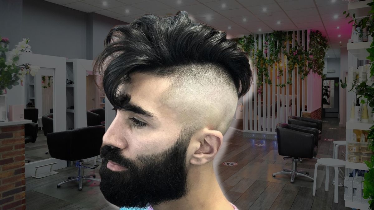 toc-mohawk-18 Người với kiểu tóc undercut nổi bật, râu rậm, trong tiệm cắt tóc hiện đại có trang trí cây xanh.