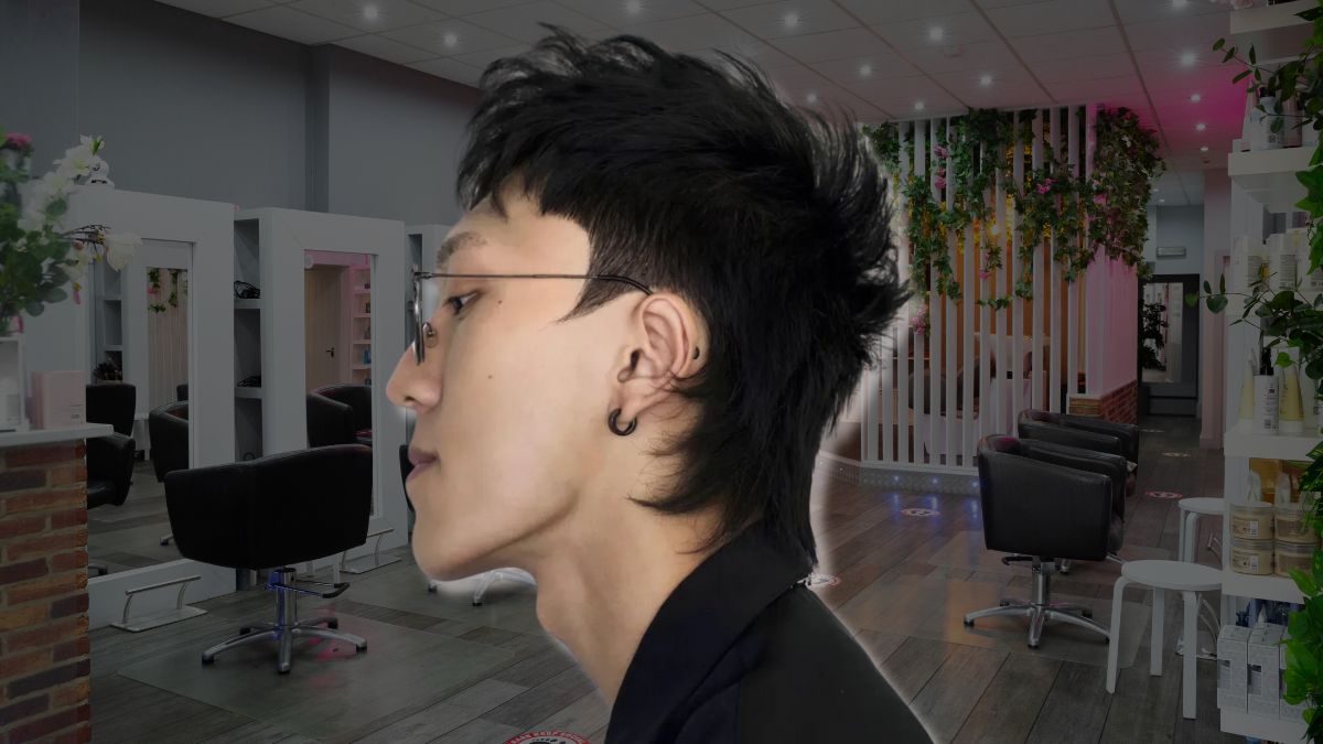 toc-mohawk-9 Người đeo kính và khuyên tai đứng trong tiệm làm tóc hiện đại với ghế và gương.