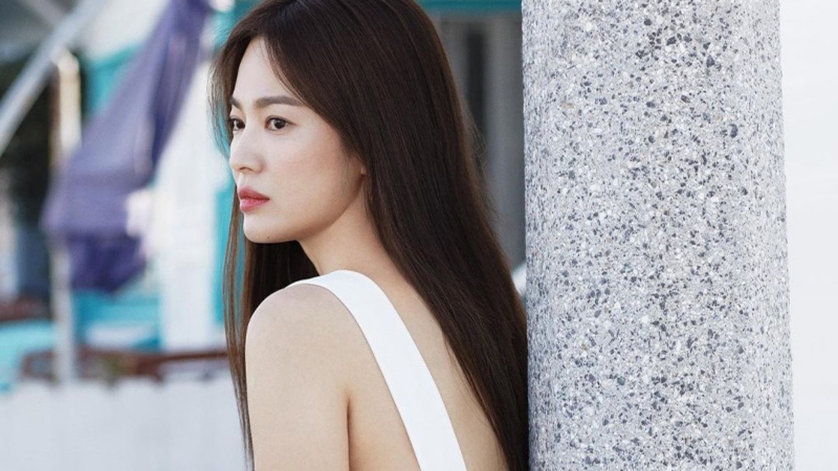 toc-song-hye-kyo-1 Người phụ nữ tóc dài đứng dựa vào cột đá, mặc váy trắng, nhìn xa xăm ra ngoài trời.