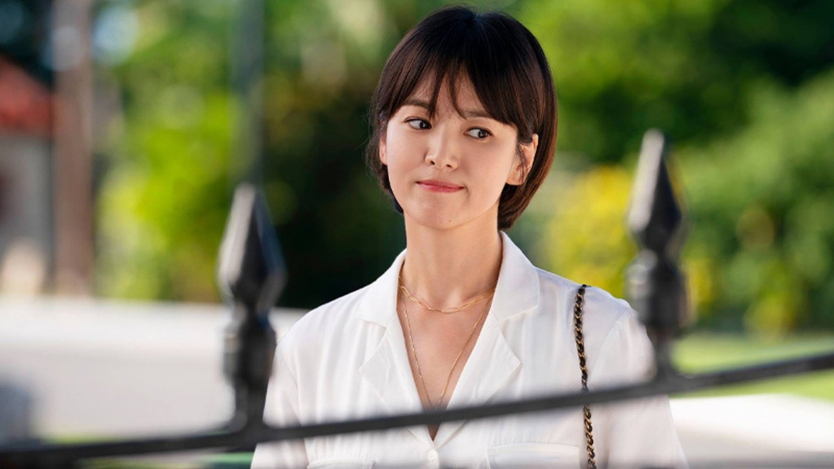 toc-song-hye-kyo-5 Người phụ nữ mặc áo trắng đứng ngoài trời, nền là cây xanh mờ ảo, ánh sáng tự nhiên chiếu lên mặt.