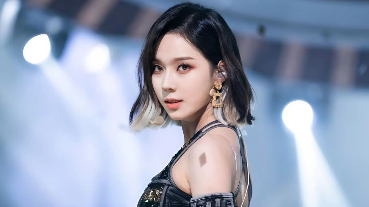 Người phụ nữ tóc ngắn, trang điểm tinh tế, mặc trang phục biểu diễn, nhìn về phía máy ảnh trên sân khấu sáng đèn.
