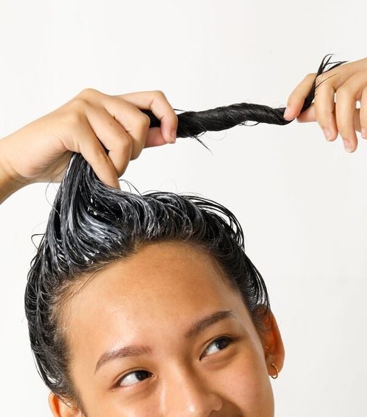 Người đang xoắn tóc có bôi chất dưỡng màu trắng, nền trắng sáng.
