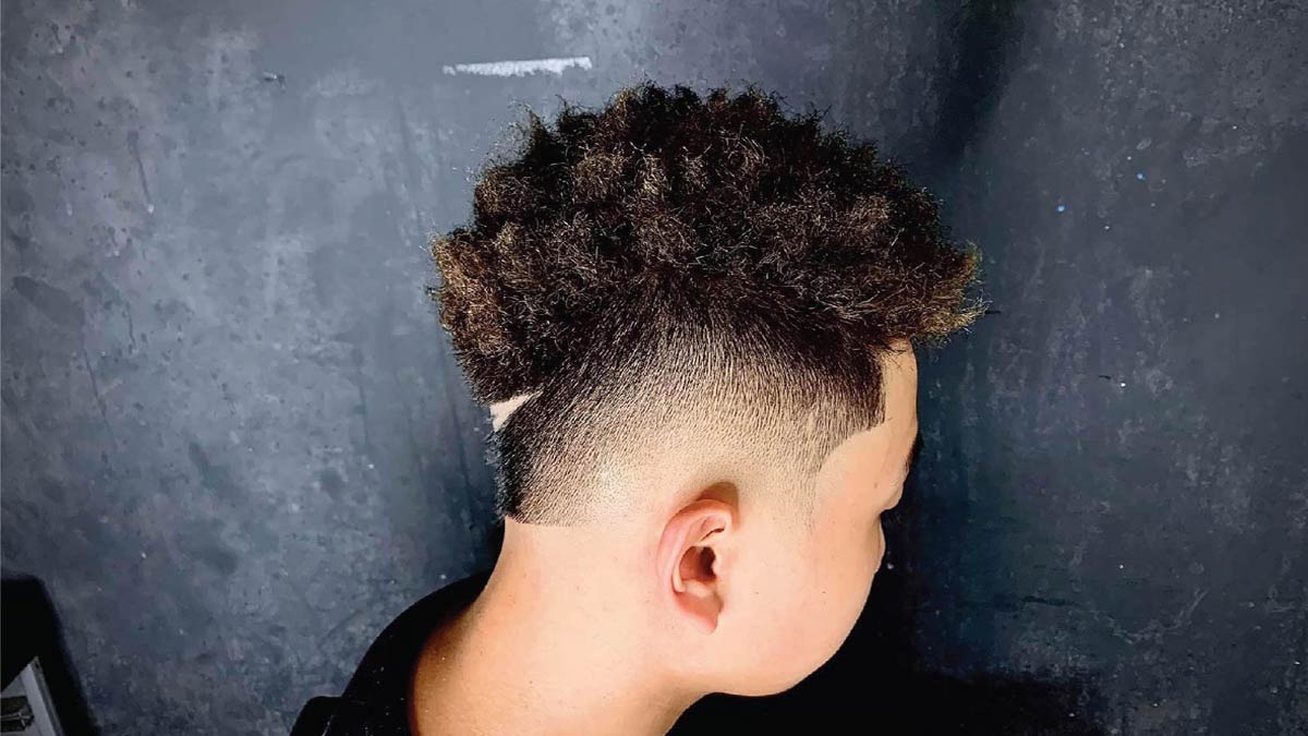 Kiểu tóc undercut với phần tóc trên xoăn tự nhiên, nền tường màu tối phía sau.