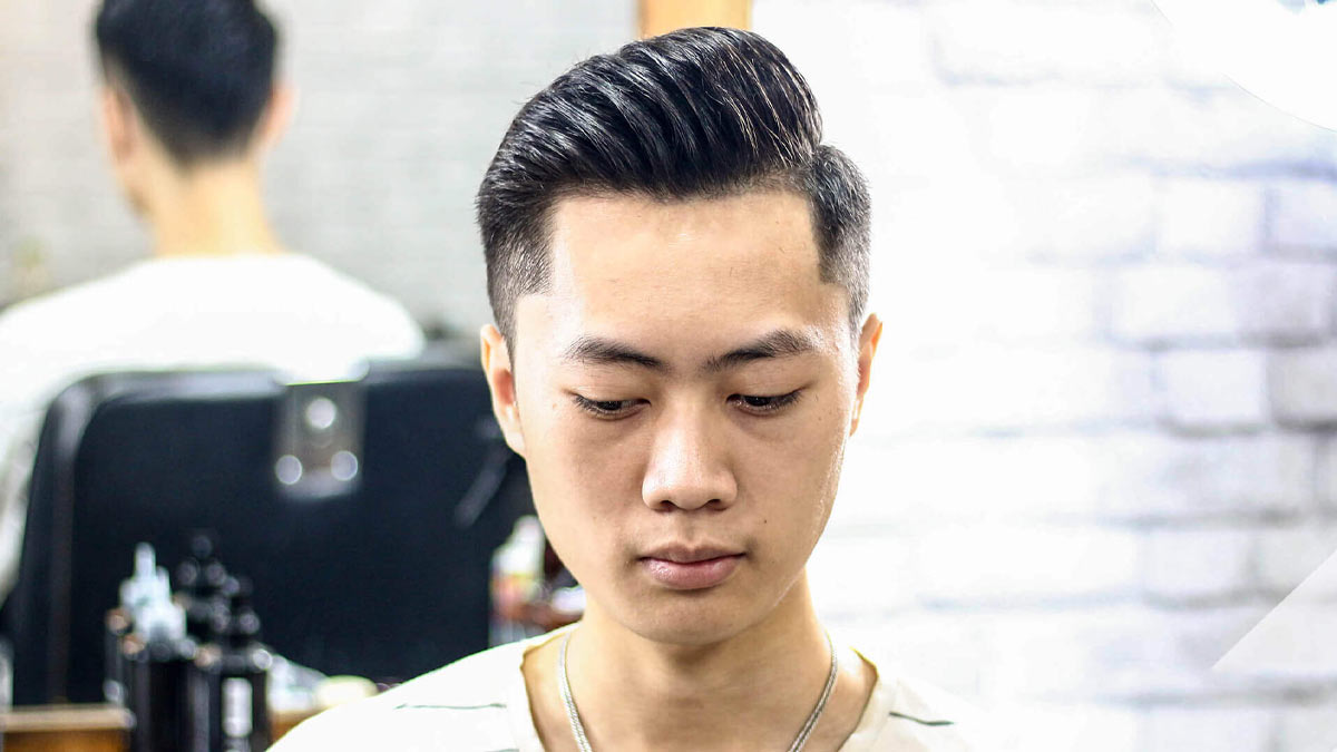 Người tóc ngắn gọn gàng ngồi trong tiệm cắt tóc, phía sau là gương và dụng cụ làm tóc.