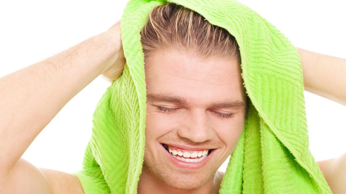Người đang mỉm cười và dùng khăn tắm màu xanh lá cây lau tóc trên nền trắng.